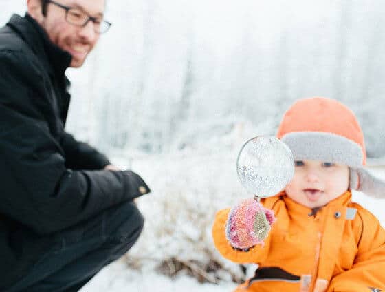 Dad plays with young child outside with a magnifying glass.